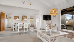 Een moderne woonkamer met een wit kleurenschema, een glazen salontafel, een witte bank en een eethoek met witte stoelen.