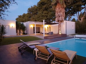 Une maison moderne dotée d’une piscine, d’un espace salon extérieur et d’une terrasse bien éclairée.