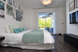 Une chambre dotée d’un grand lit, d’une télévision et d’un balcon offrant une vue sur la verdure.