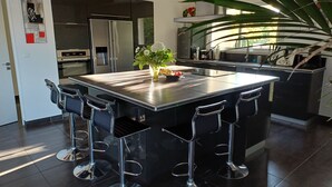Une cuisine moderne dotée d’un îlot central, de tabourets de bar, d’appareils électroménagers en acier inoxydable et d’une grande plante en pot.