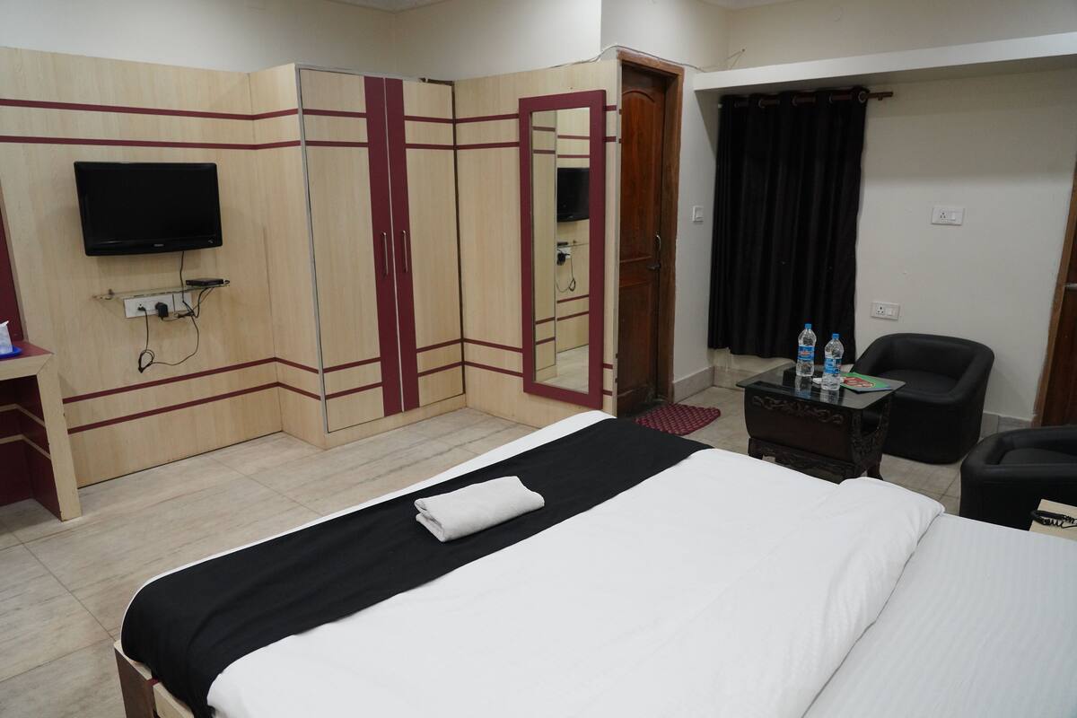 A hotel room with a bed, a TV mounted on the wall, a wardrobe, a desk, and a chair.