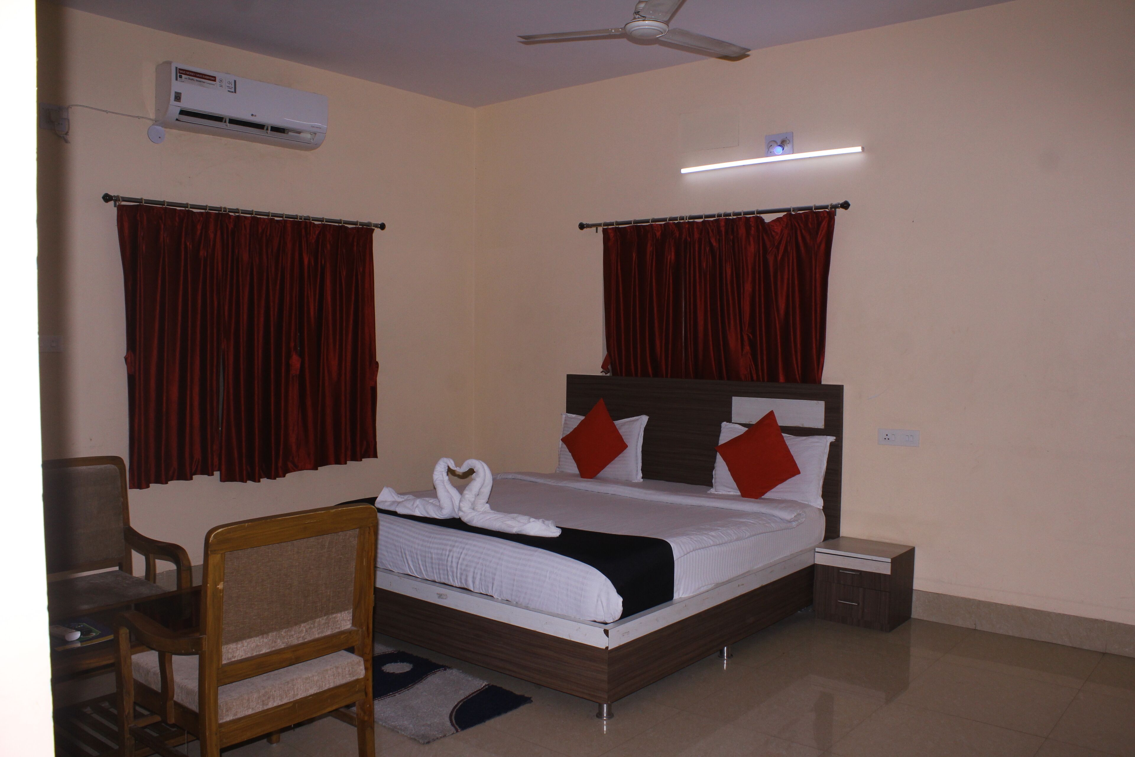 Habitación de hotel con cama, escritorio, silla, aire acondicionado, ventilador de techo y mesita de noche.
