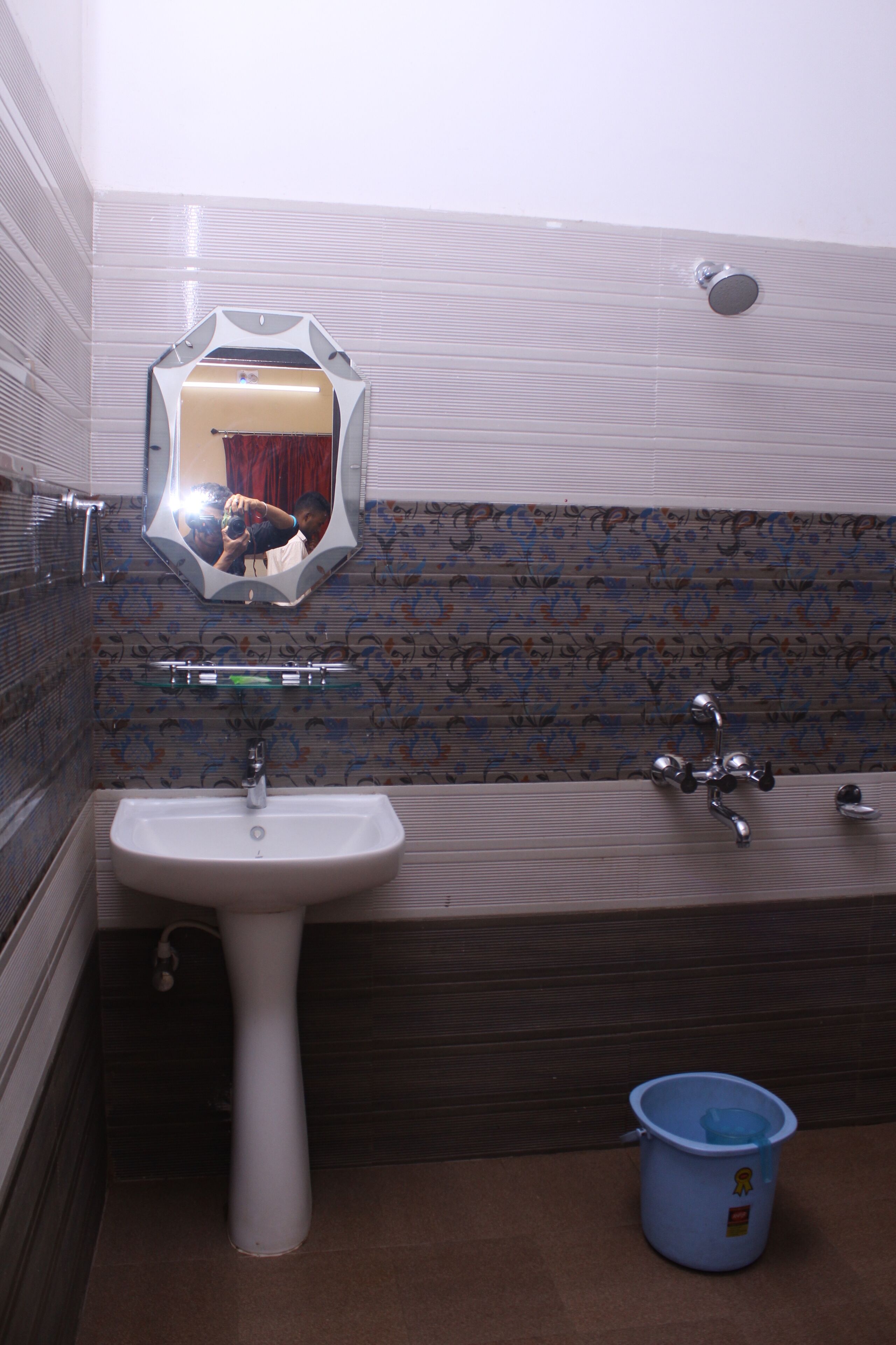 Un baño con un lavamanos blanco, un espejo, una bañera y un cubo azul.