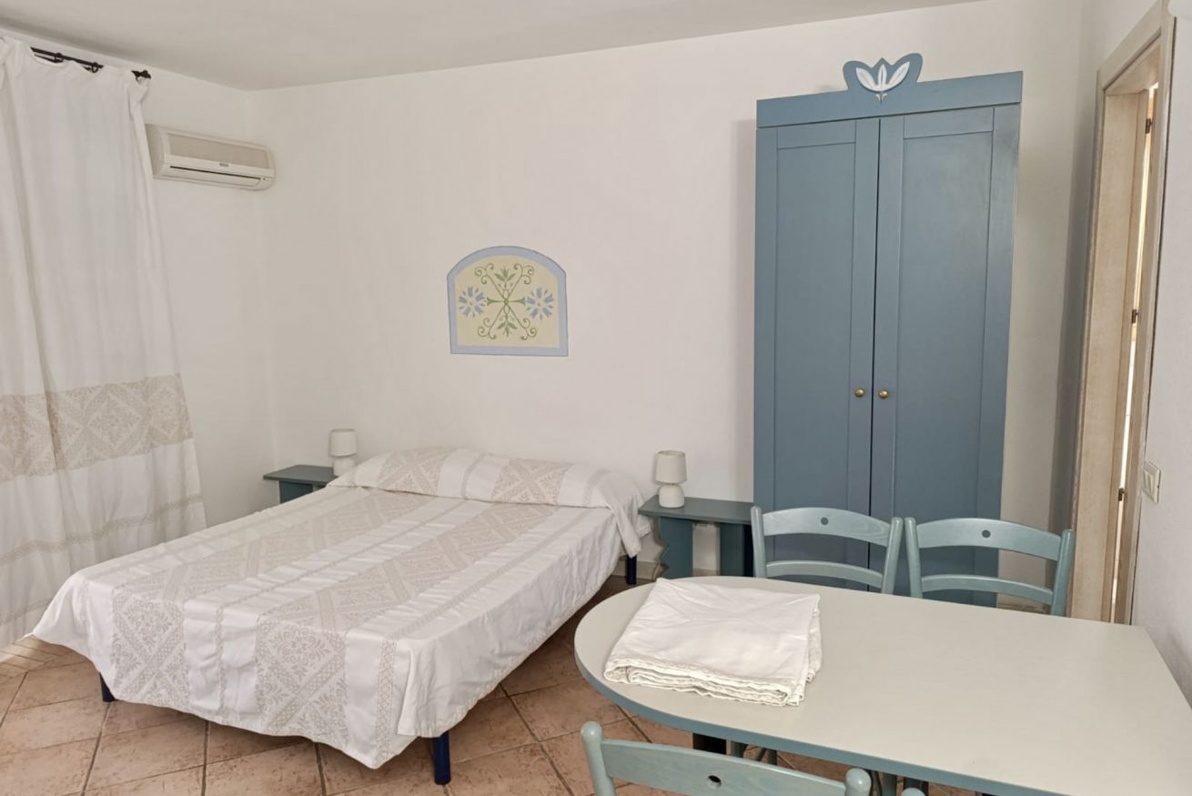 A bedroom with a bed, a table, chairs, a wardrobe, and a wall decoration.