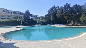 Una piscina grande y clara con un borde de baldosas, rodeada de árboles y un edificio con tejado de cerámica.