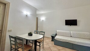 Una habitación pequeña y limpia con una mesa de comedor, sillas, un sofá y un televisor montado en la pared.