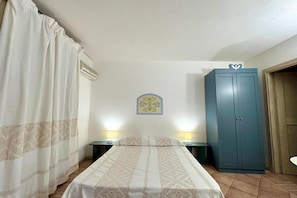 Un dormitorio con cama, dos mesitas de noche con lámparas, un armario, una cortina y un equipo de aire acondicionado.