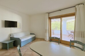 A room with a sofa, a table, chairs, a TV, and a sliding glass door to an outdoor area. - Charming three-room apartment of approximately 60 square meters with a 25 square meter covered veranda, located on the ground or first floor.It comprises a living room with a fully equipped kitchenette and a sofa bed, a bedroom with a double bed, a secon (Porto Rotondo)