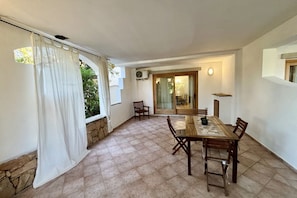 Un espace repas avec une table et des chaises en bois, un mur en pierre et une vue sur la verdure à l’extérieur.