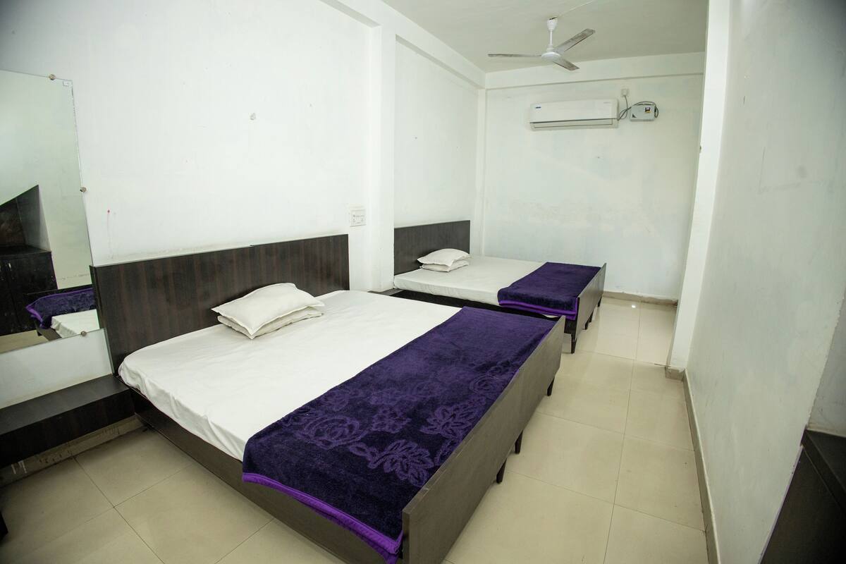 A hotel room with two single beds, a ceiling fan, an air conditioning unit, and a mirror.