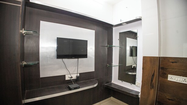 A modern bathroom with a dark wood vanity, a mounted TV, and a mirror. - Sri Residency (Ujjain)