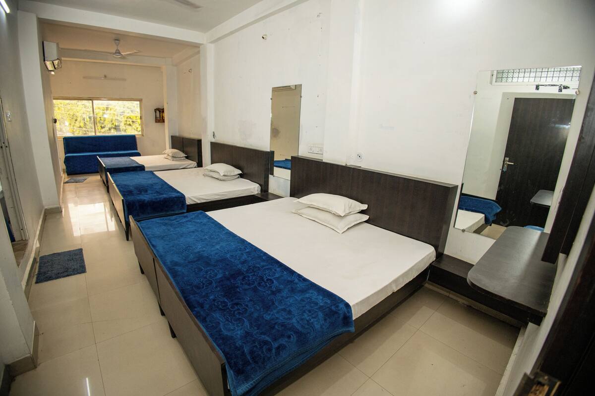 A hotel room with three single beds, a bathroom with a mirror and sink, and a window with a view.