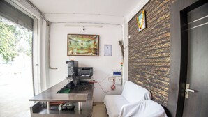 A room with a reception desk, a computer, a printer, a couch, and a wall with a decorative panel. - Sri Residency (Ujjain)