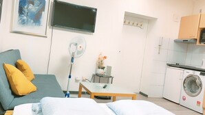 Ein modernes, helles Zimmer mit einem Bett, einem Schreibtisch, einer Waschmaschine und einem Fernseher.