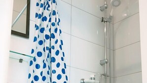 Eine Dusche mit weißer Duschvorhang, verziert mit blauen Punkten, einer Handbrause und einem am Wand montierten Wasserhahn.