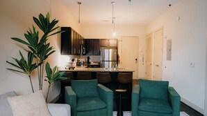 A compact living space with a kitchenette, two green armchairs, a sofa, and a large plant. - Downtown Loft • Balcony • King Bed • Stylish Stay (Motgomery)