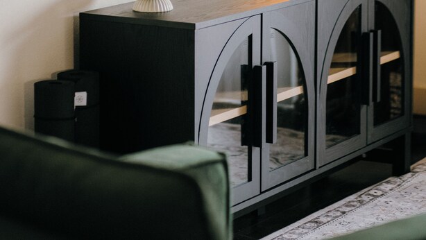 A modern living room with a flat-screen TV mounted on the wall, a dark wooden console table with a white bowl and two candles, and a green armchair. - Downtown Loft • Balcony • King Bed • Stylish Stay (Motgomery)