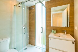 Ein modernes Badezimmer mit einer gläsernen Dusche, einem weißen Waschbecken und einer Holzvertäfelung.