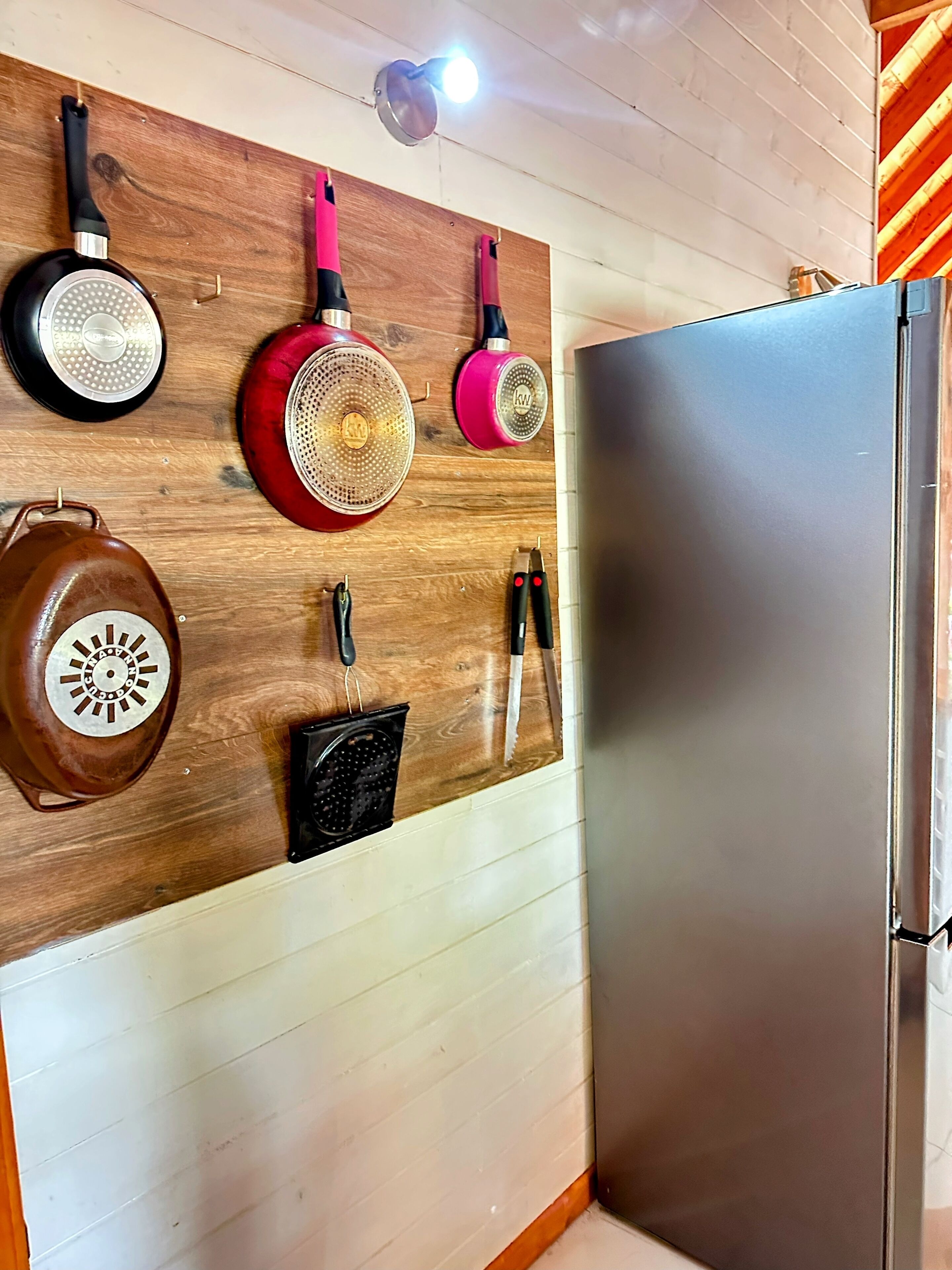 Una cocina con un estante de madera montado en la pared que contiene diversos utensilios y utensilios de cocina.