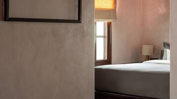 A hotel room with a bed, a framed picture on the wall, a window with a view of a building, and a lamp on the nightstand.