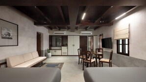 A modern hotel room with a sofa, a dining table with chairs, a TV, and a kitchen area. - Delhi House (Puducherry)