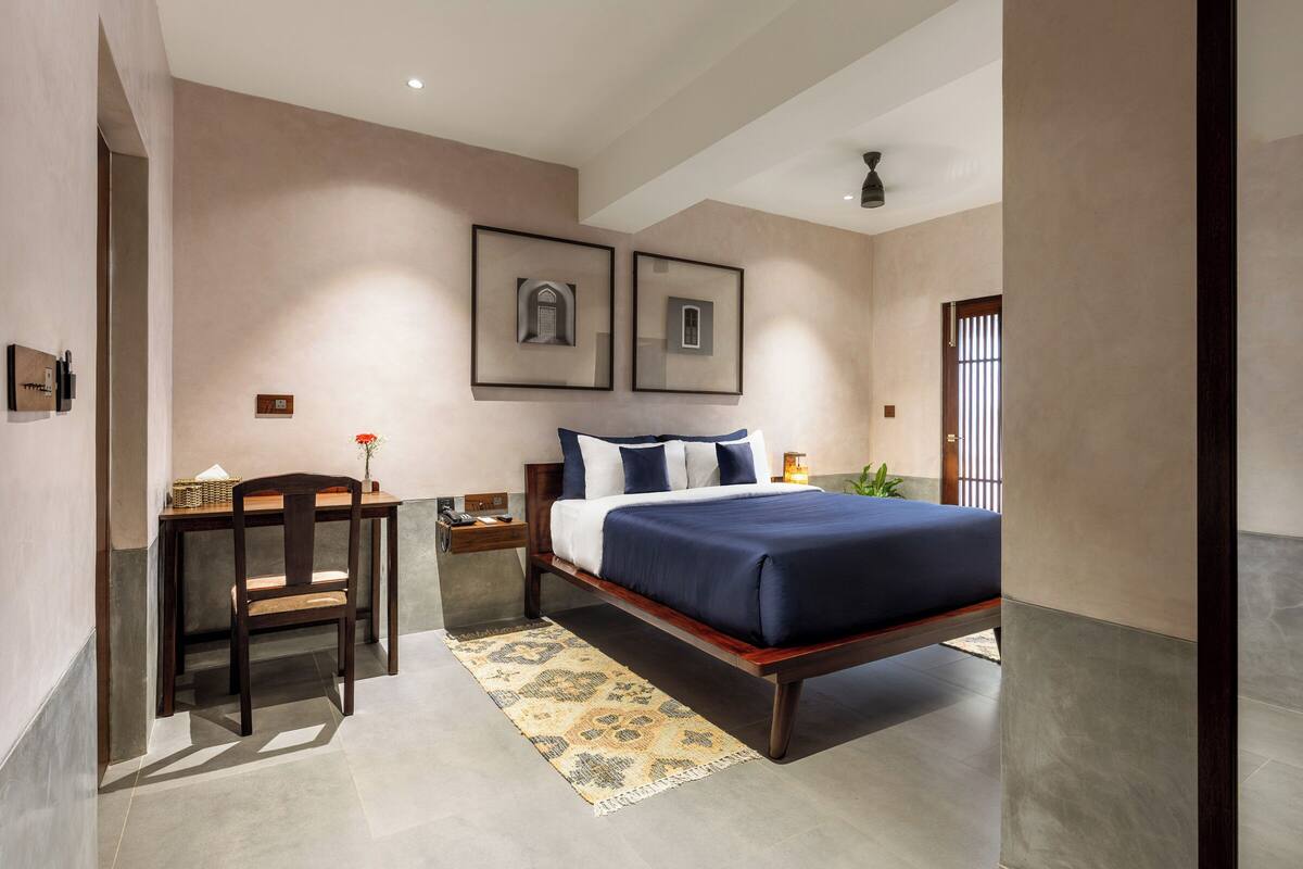 A bedroom with a bed, a desk, and a chair. There are two framed pictures on the wall.