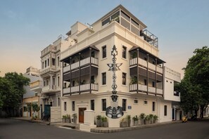 A multi-story building with balconies, a central decorative element, and potted plants. - Delhi House (Puducherry)