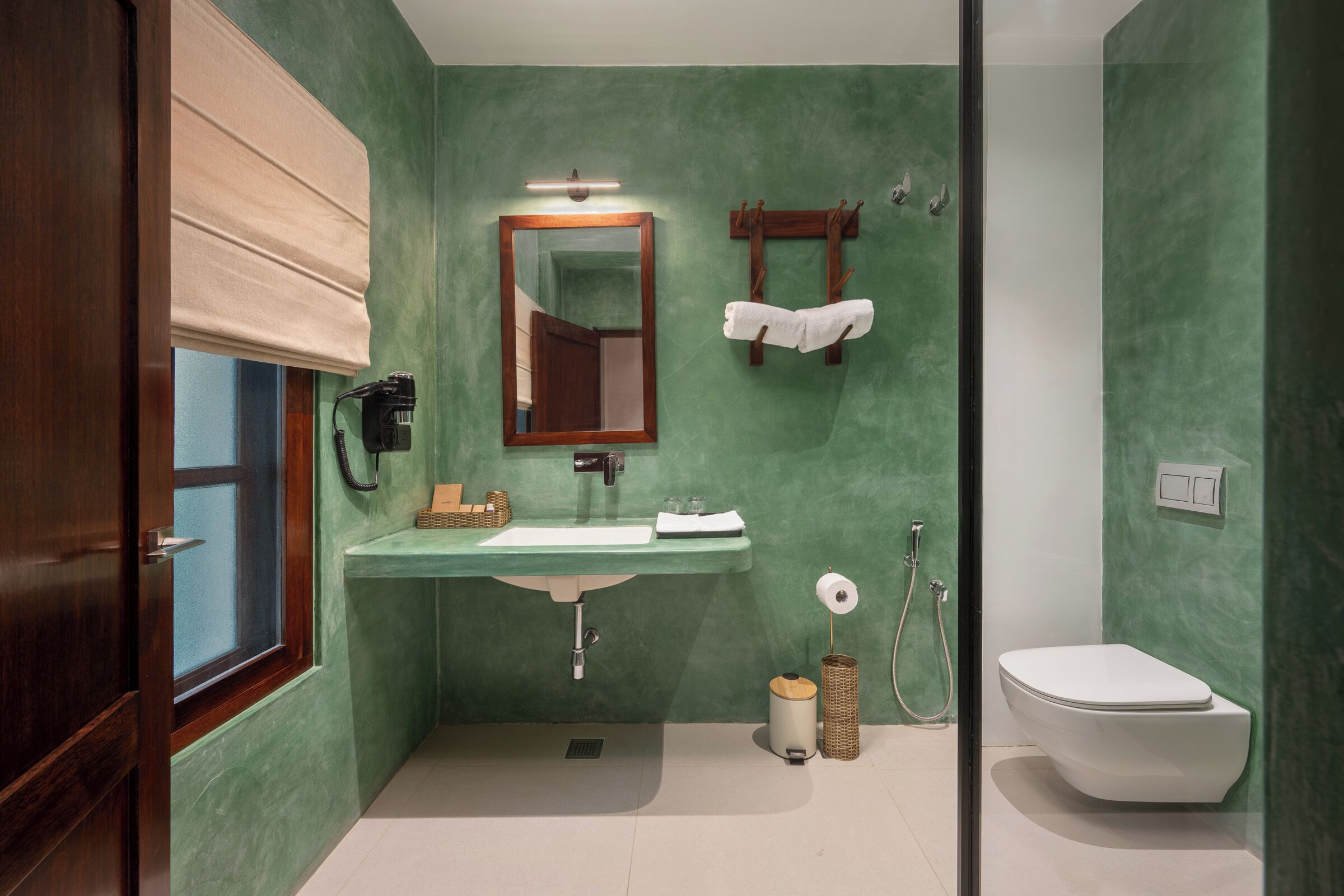 A bathroom with a green wall, a wooden door, a sink with a mirror, a toilet, and a towel rack.