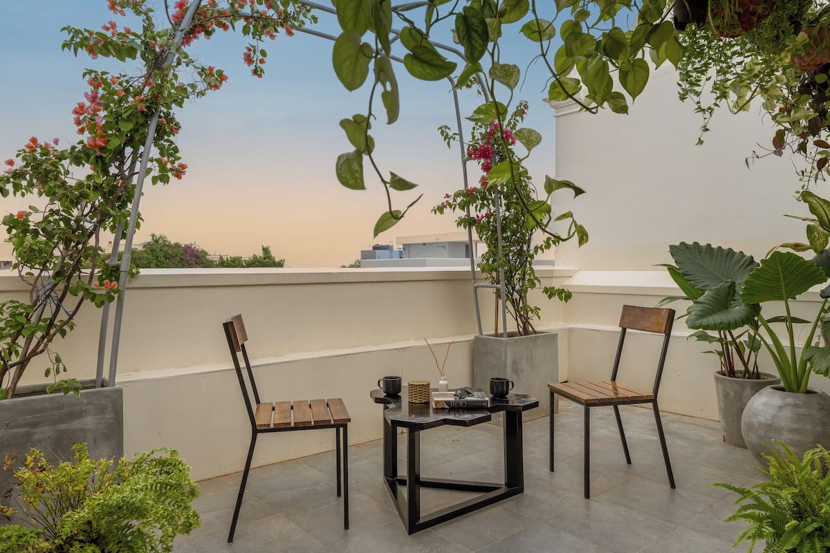 A rooftop terrace with two wooden chairs, a small table, and potted plants.