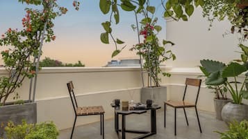 Una terraza en la azotea con dos sillas de madera, una mesita y plantas en macetas.