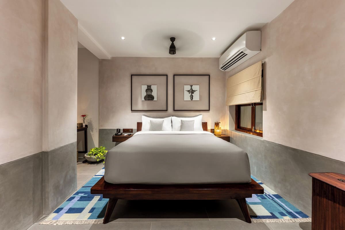 A modern hotel bedroom with a large bed, framed artwork on the wall, and a small side table.