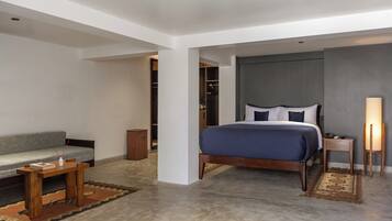 Una habitación de hotel moderna con una cama grande, una mesita de noche de madera, un pupitre junto a la cama, un sofá y una pequeña mesa con un jarrón.