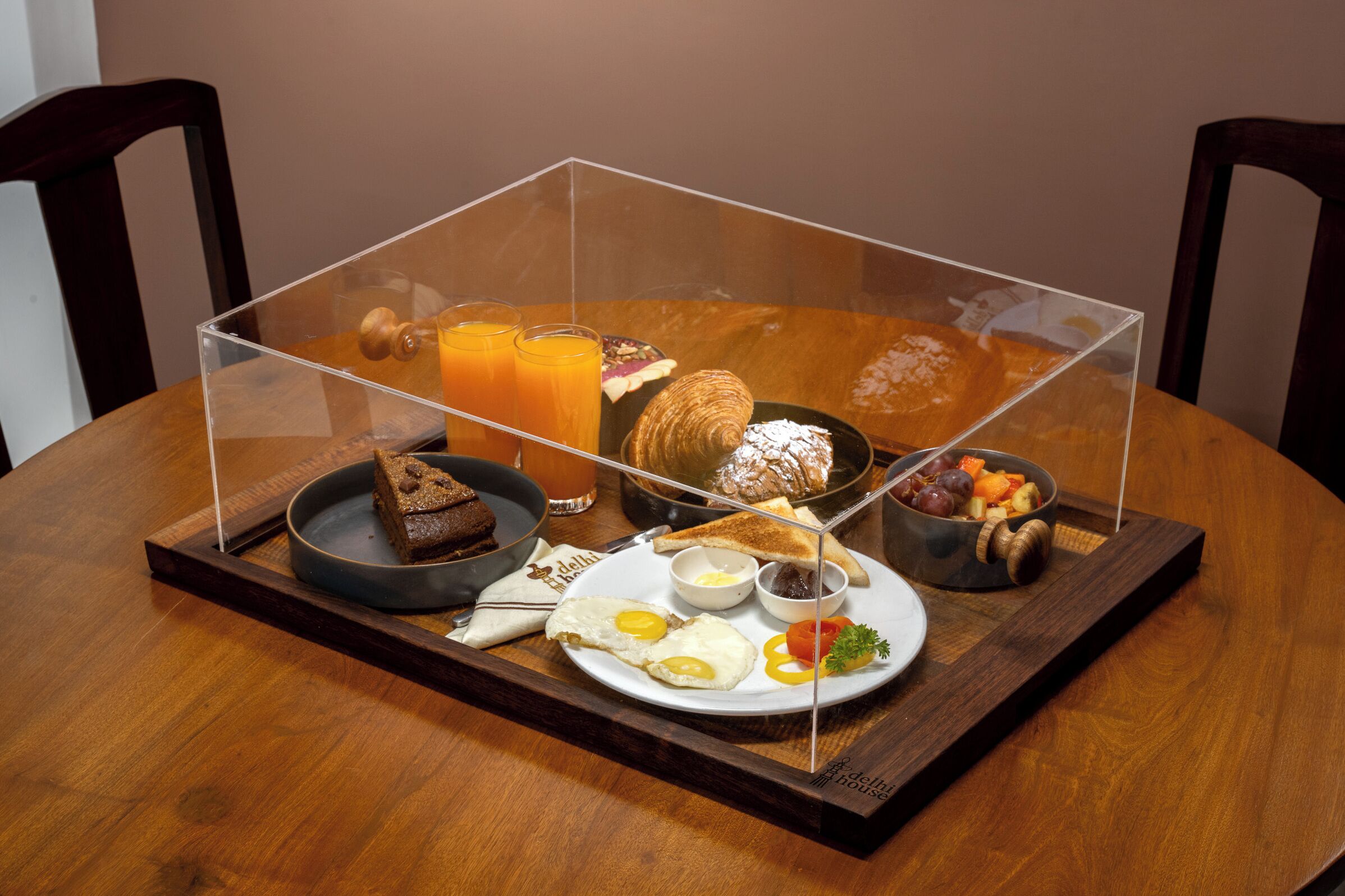 A breakfast tray with eggs, toast, fruit, and juice on a wooden table.
