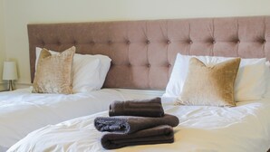 A neatly made bed with a tufted headboard, two pillows, and folded towels. -  Hillside House , 18th century secluded country house with hot tub & gardens. (Dunfermline)