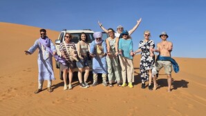 Un grupo de personas de pie en un desierto, con un vehículo al fondo.