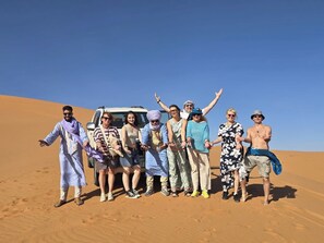 A group of people standing in a desert with a vehicle in the background. - campground in Merzouga for a memorable stay (Merzouga)