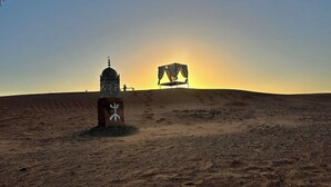 Paisaje desértico con una estructura parecida a una tienda de campaña y un pequeño edificio con cúpula y minarete.