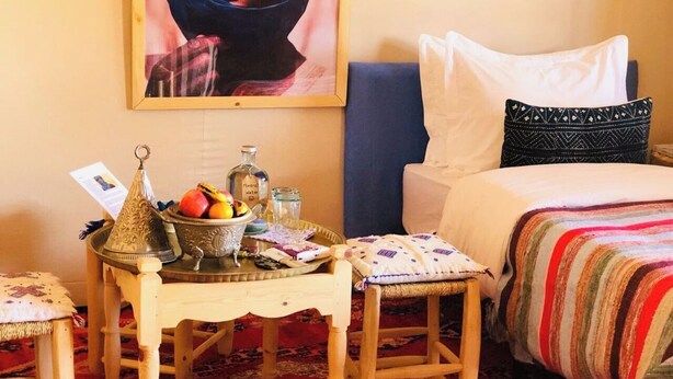Una habitación con una cama, una mesita con un frutero, una botella y un adorno.