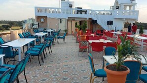 Un área de comedor al aire libre con mesas y sillas, una escalera que conduce a un edificio y vistas del paisaje circundante.