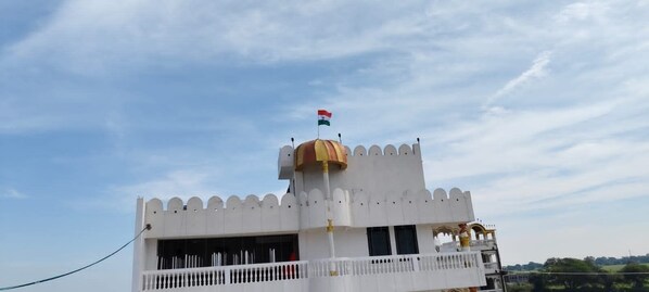 Un edificio con fachada blanca, una pequeña torre con una bandera y un balcón.