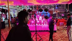 Un espacio interior para eventos, bien iluminado, con mesas cubiertas de manteles rosas y un escenario con instrumentos musicales.