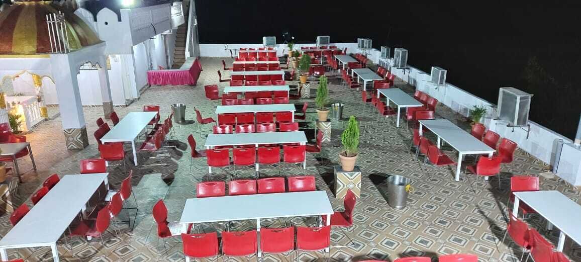 An outdoor dining area with multiple tables and red chairs, surrounded by a patterned floor and white walls.