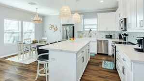A modern kitchen with white cabinetry, a central island, and pendant lighting. - Lake2Sea - Spacious Retreat, Gulf & Waterway View! (Surfside Beach)