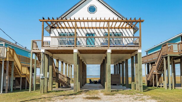 A two-story wooden structure with a balcony, supported by stilts, overlooking a beach. - Lake2Sea - Spacious Retreat, Gulf & Waterway View! (Surfside Beach)