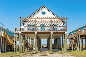 Ein zweistöckiges Holzgebäude mit Balkon, das auf Stelzen über einen Strand ragt.