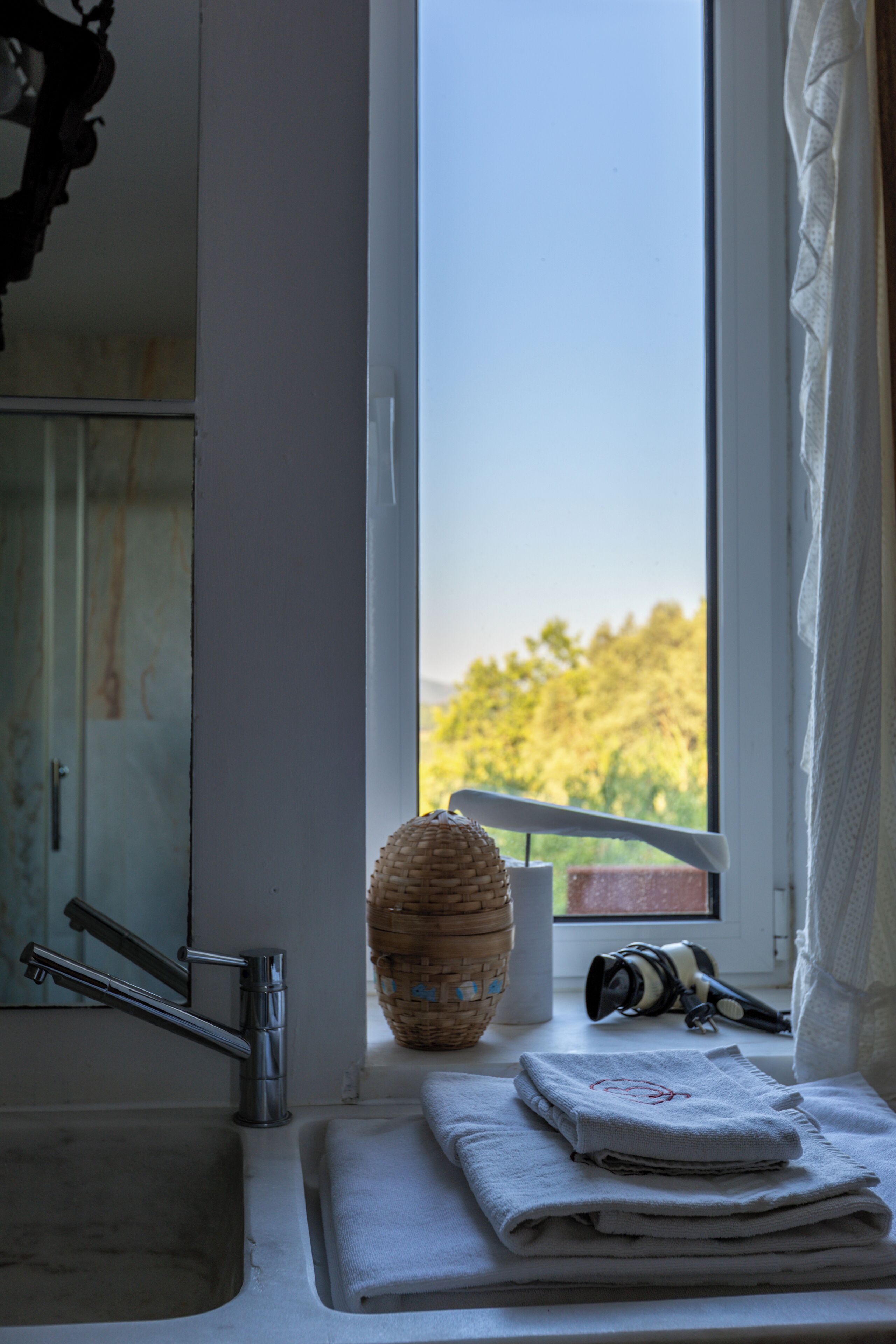 A bathroom with a sink, a mirror, a window with a view of trees, and a towel rack with towels.