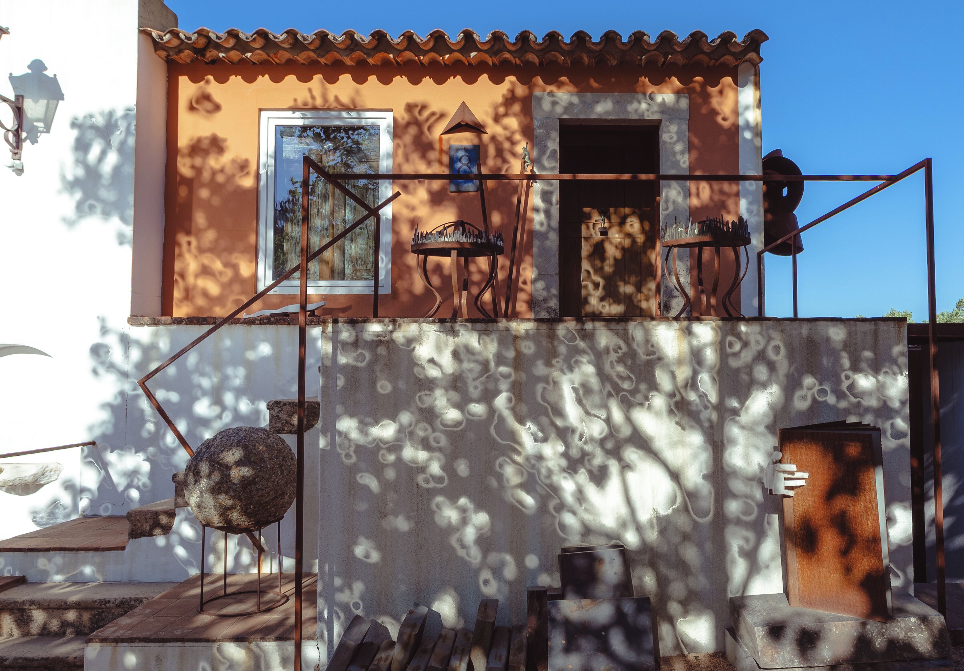 A building with a tiled roof, a door, and a window. There are metal structures and a stone sculpture on the ground.