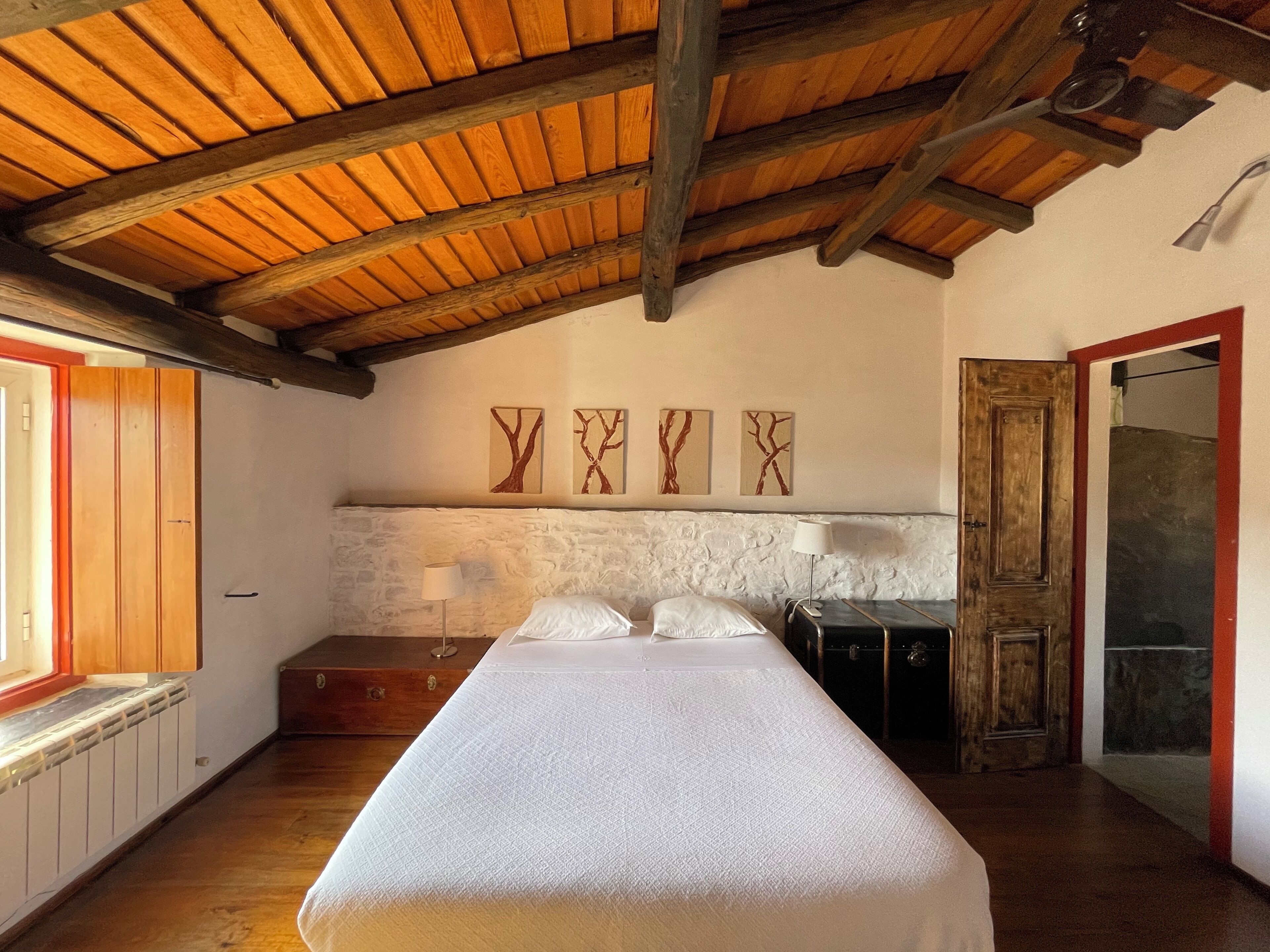 A bedroom with a wooden ceiling, a bed, a dresser, a mirror, and artwork on the wall.