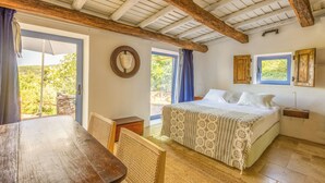 Ein Schlafzimmer mit einem großen Bett, Holzbalkendecke, Blick durch eine Tür und einem kleinen Tisch mit Stühlen.