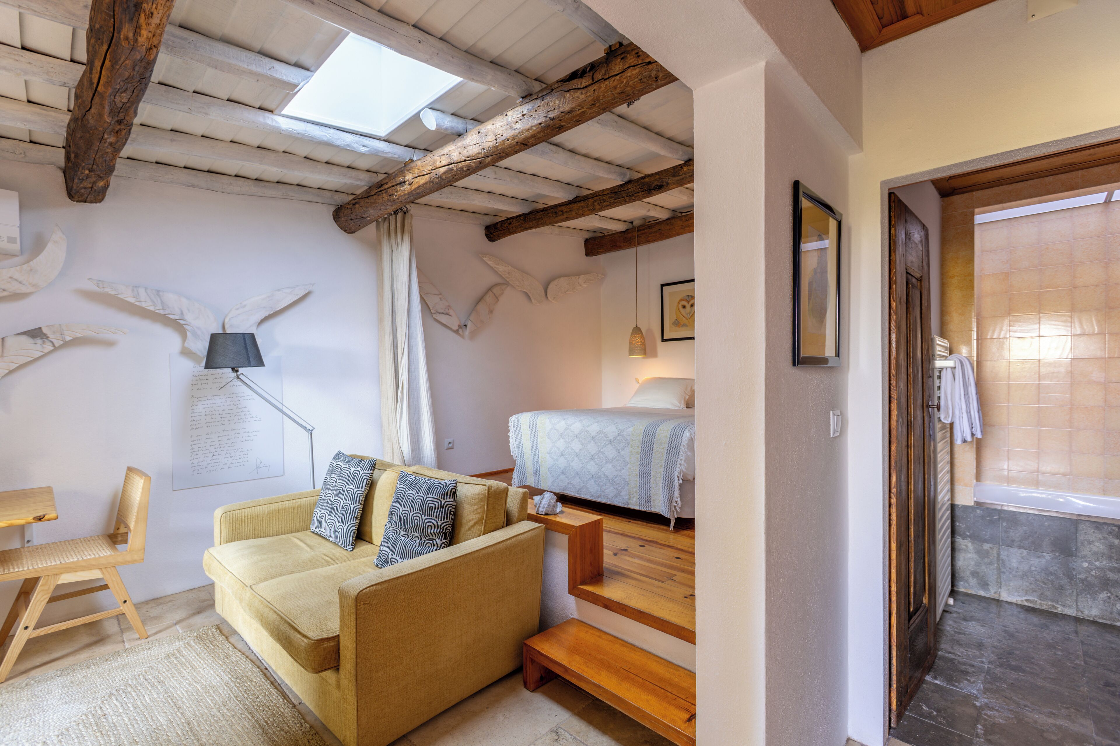 A cozy room with a sofa, a wooden bench, a bed, and a skylight.